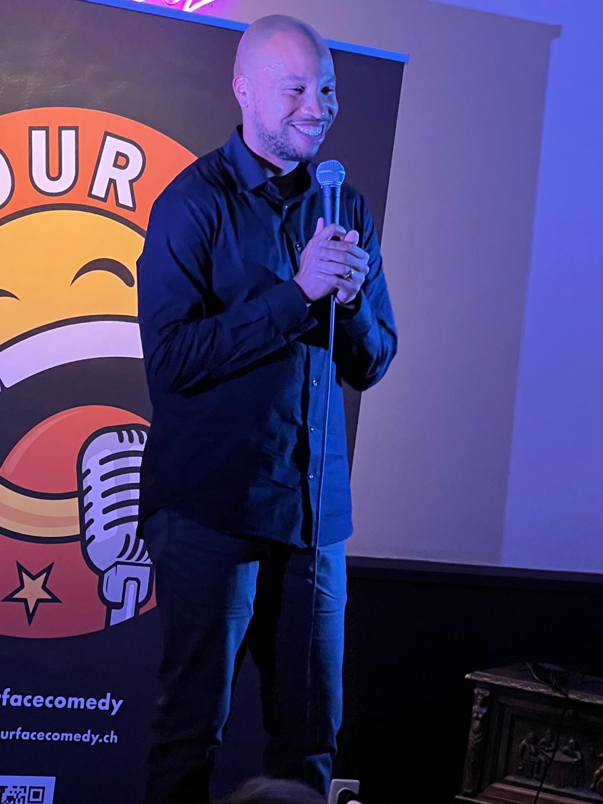 IN YOUR FACE Comedy, a comedian performing stand-up with a microphone on stage in Zürich (2024)