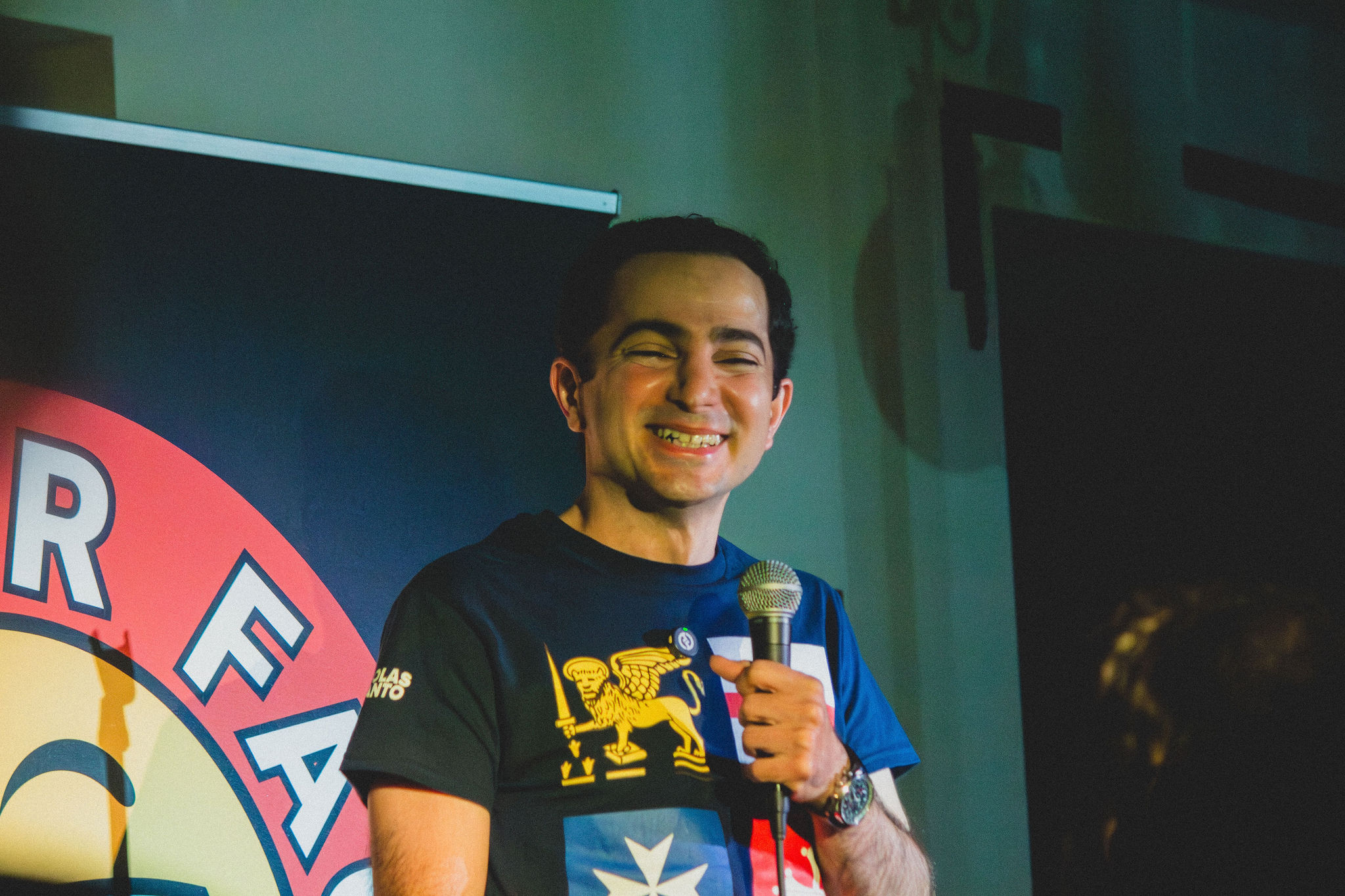 IN YOUR FACE Comedy, a comedian performing stand-up with a microphone on stage in Zürich (2026)